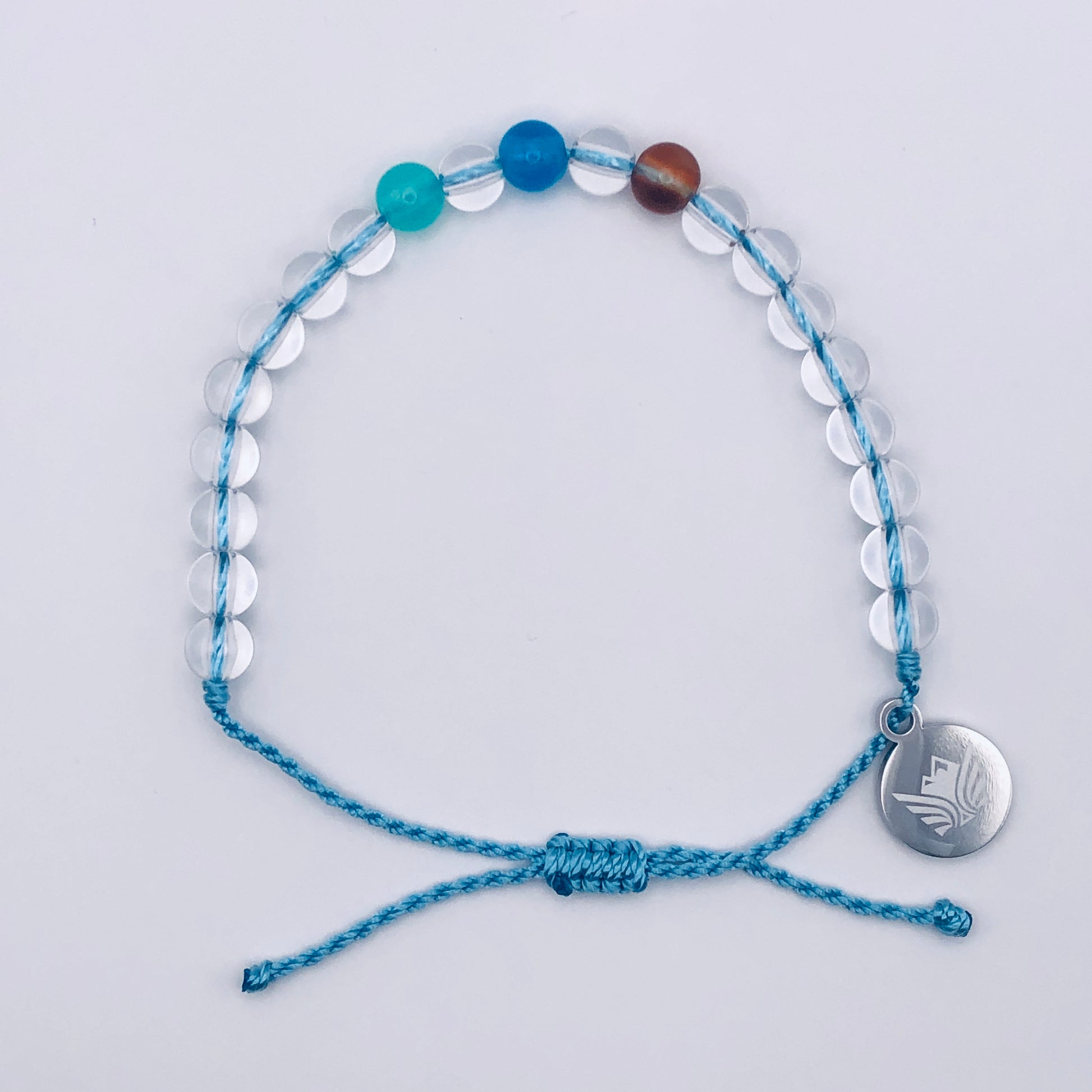 Blue beaded bracelet with a silver charm on a light gray background